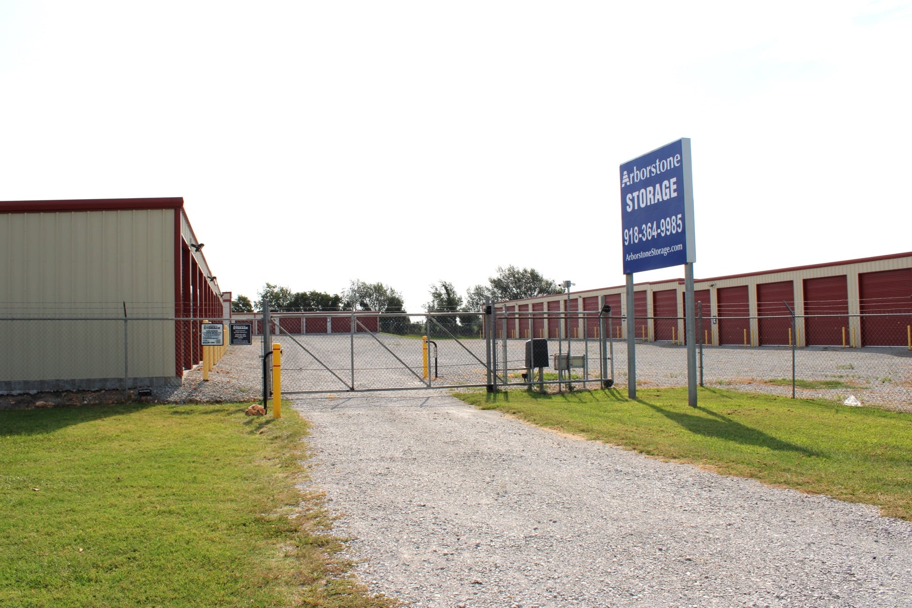 Ground-level view of Arborstone Storage Monkey Island showing tan and blue drive-up units with the Arborstone Storage sign visible at the gate on OK-125.