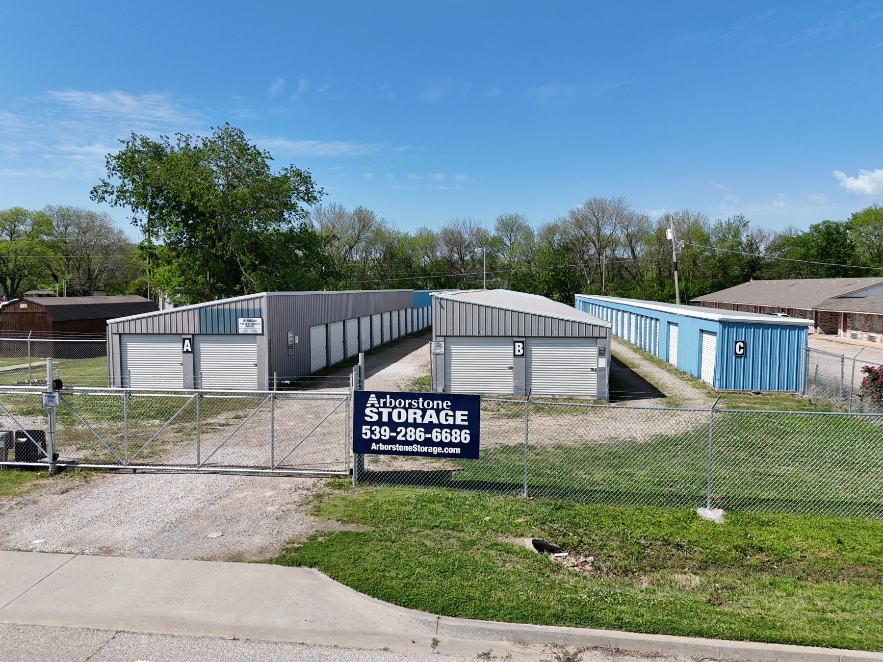 Ground-level view of Arborstone Storage Henryetta II showing drive-up units with roll-up doors and the Arborstone Storage sign at the gate.