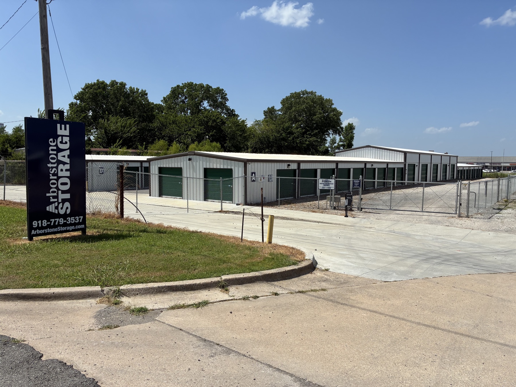 Ground-level view of an Arborstone Storage facility in Muskogee, OK, with the Arborstone Storage sign and phone number visible at the gate.