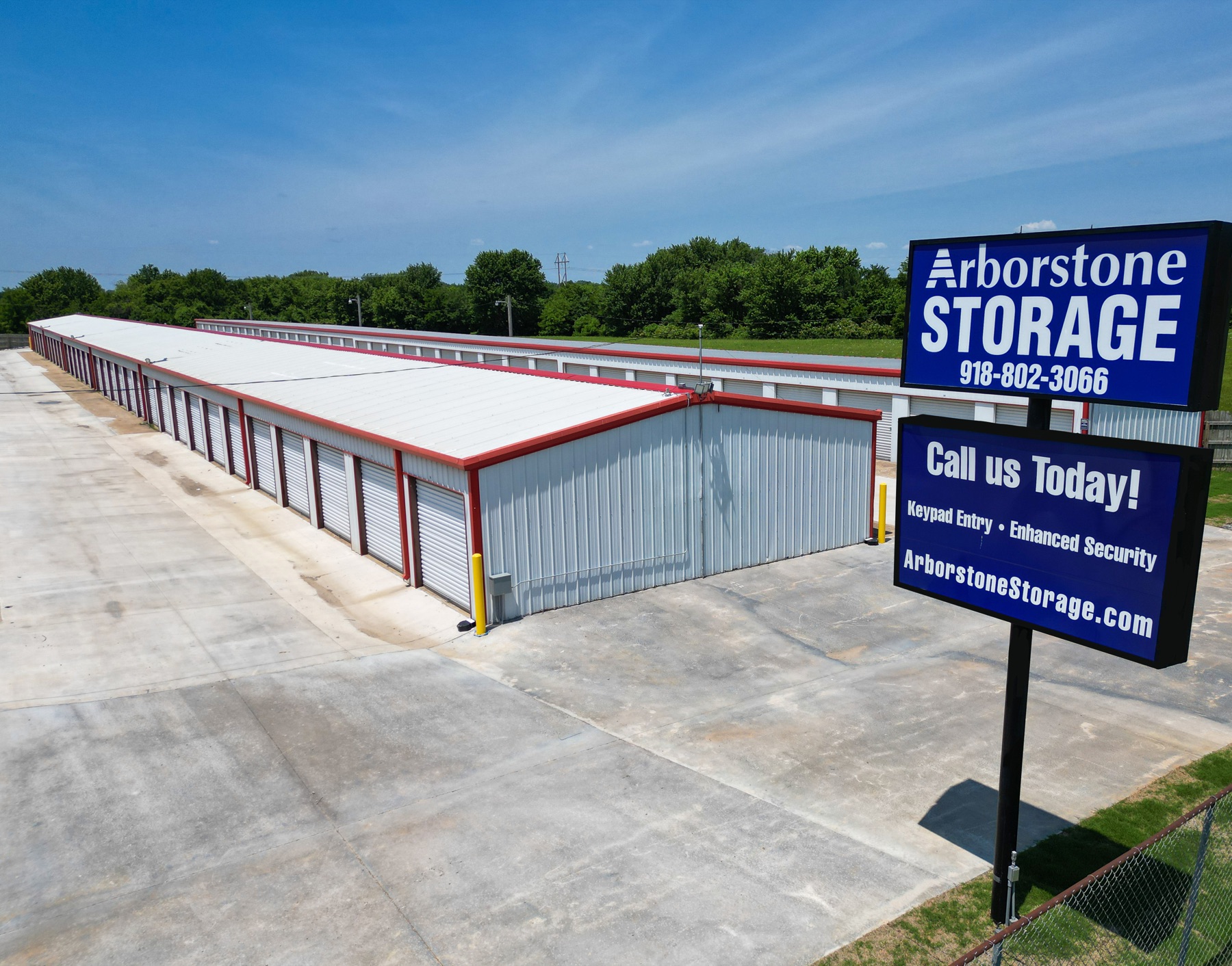 Aerial view of Arborstone Storage Wagoner I showing long rows of drive-up units with red trim, gravel drive, and the Arborstone Storage sign at the entrance.