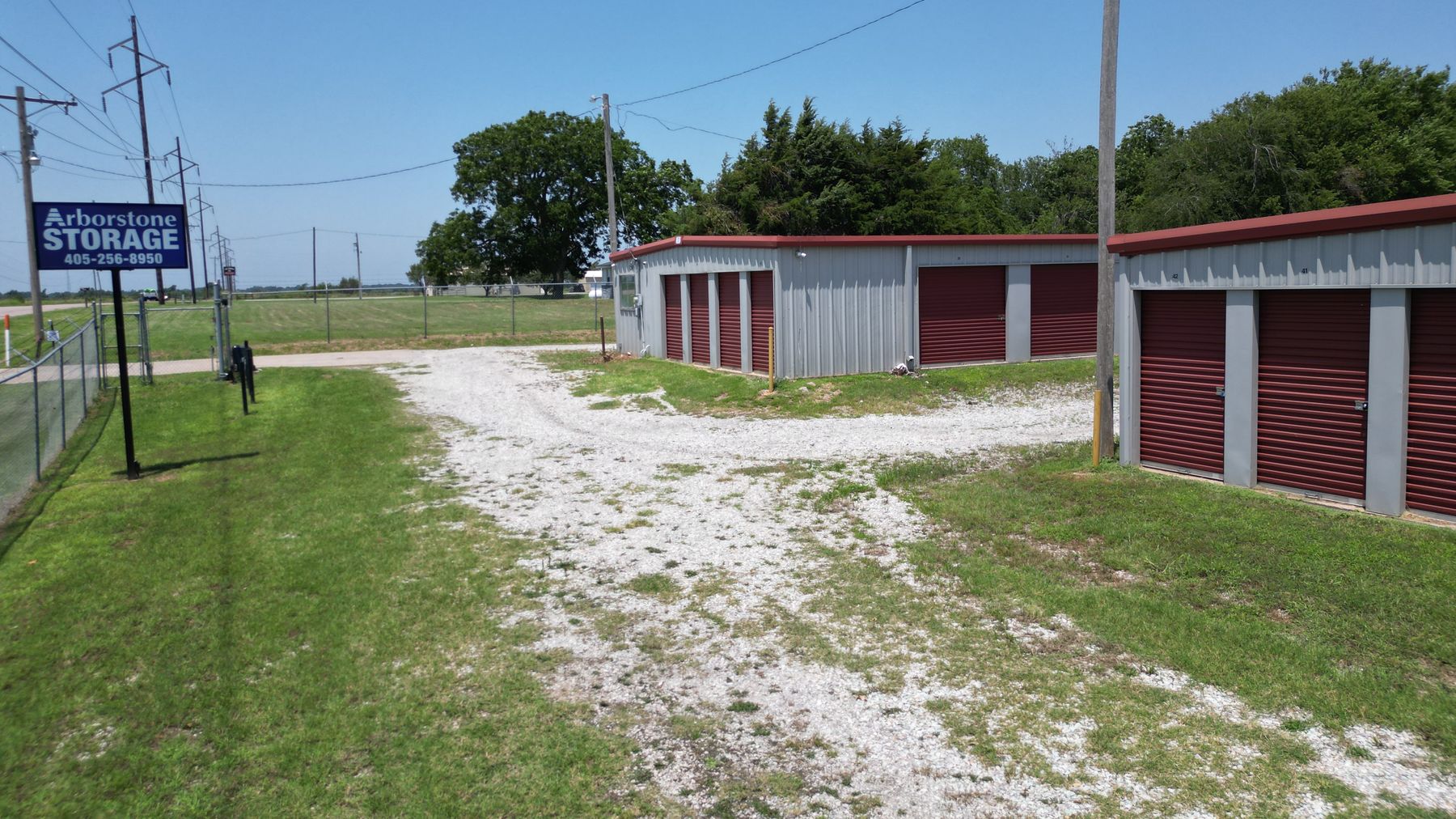 Arborstone Storage Shawnee: the blue Arborstone Storage sign by the fenced entrance, a gravel drive and drive-up storage buildings with red roll-up doors.