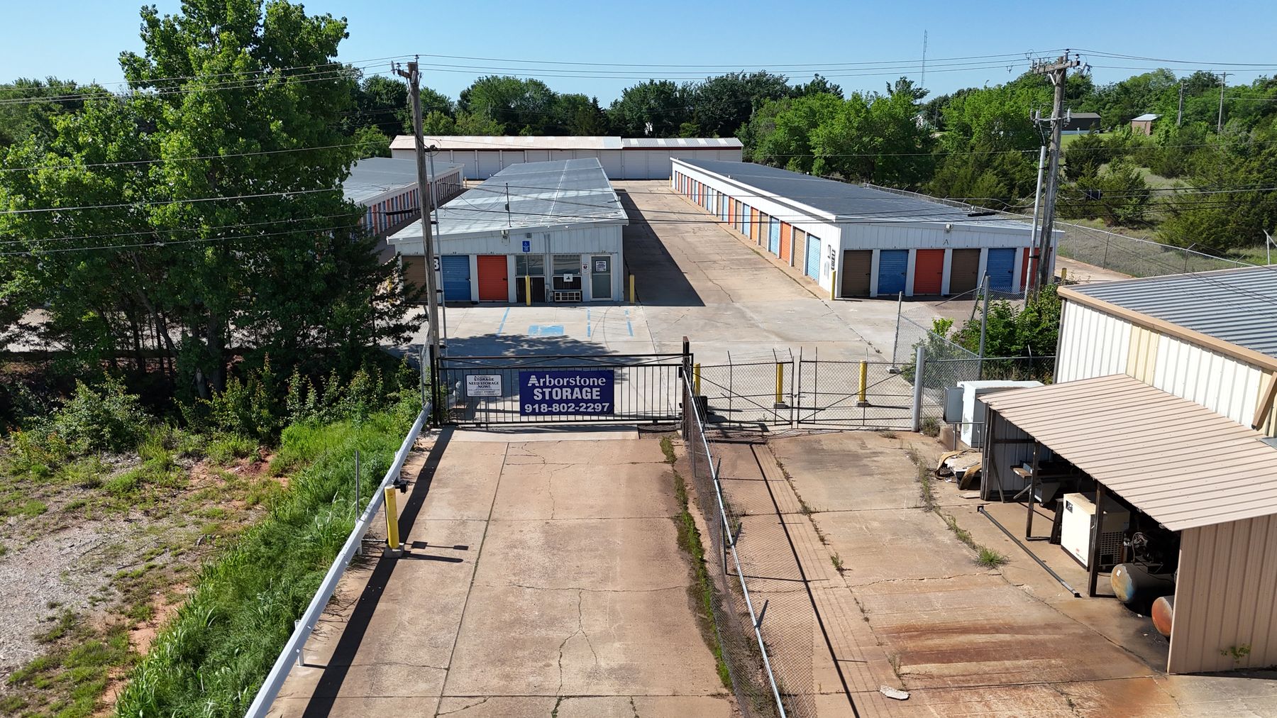 Aerial view of Arborstone Storage Stillwater: the gated entrance with the Arborstone Storage sign and drive aisles lined with orange and blue roll-up doors.
