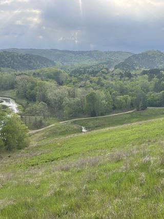 Green hillsides and wooded ridges of the Ouachita foothills near Broken Bow Lake, above a wooded valley with water at its edge.