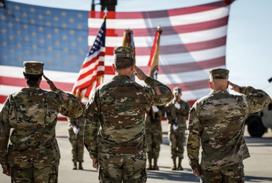 Service members in uniform saluting in front of an American flag