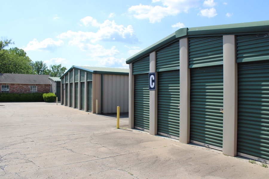 Exterior storage buildings with green roll-up doors along a paved drive aisle