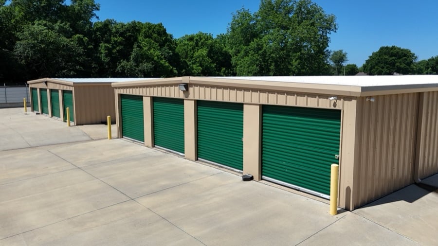 A row of drive-up storage units with green roll-up doors at an Arborstone Storage facility