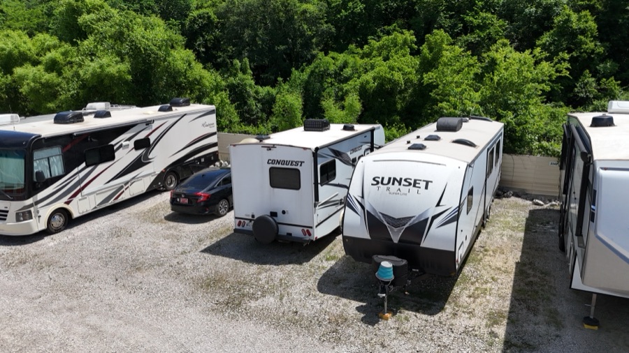 A motorhome and travel trailers parked in a gated RV storage lot