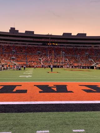 Boone Pickens Stadium at Oklahoma State University at dusk, seen from the end zone, with the stands full of fans in orange.