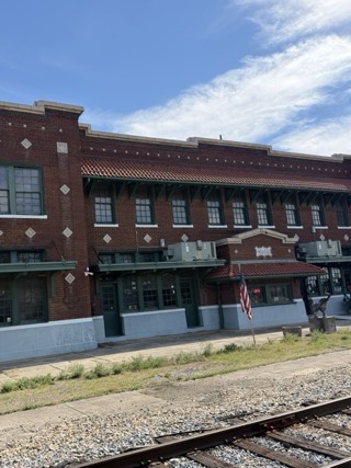 The red-brick Frisco Depot in Hugo, with its "HUGO" sign, tile-roofed awnings and the railroad tracks in front.